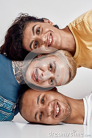 Closeup portrait of three cheerful diverse friends smiling at camera, laying head on each other, posing isolated over Stock Photo