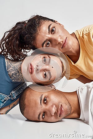 Closeup portrait of three diverse friends looking at camera, laying head on each other, posing isolated over light Stock Photo