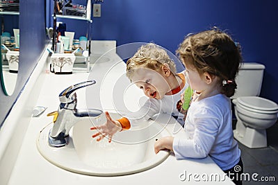 Closeup portrait of twins kids toddler boy girl in bathroom toilet washing face hands brushing teeth with toothbrash Stock Photo