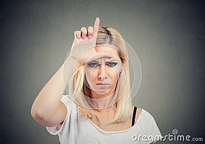 Portrait unhappy woman giving loser sign on forehead, looking at you with anger and hatred on face Stock Photo