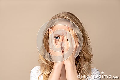 Closeup portrait woman covering hand on face, peeping with one eye. Isolated on beige wall. Stock Photo