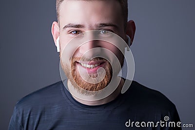 Closeup portrait of a young bearded guy of twenty-five years old, smiling, looking at the camera. In wireless white headphones. Stock Photo