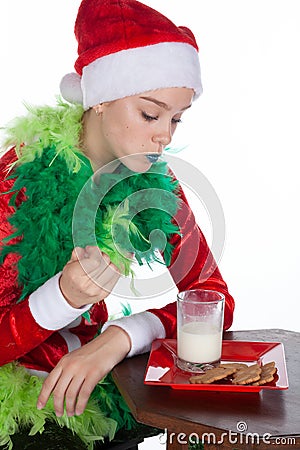 Closeup portrait of young girl wearing red santa clause hat mouthful of biscuit looking at milk Stock Photo