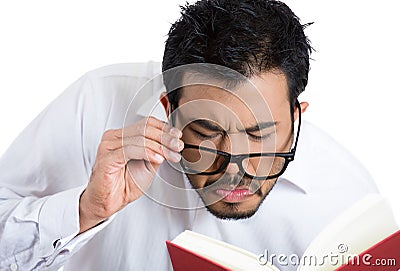 Portrait of a young nerdy guy with eye glasses trying to read book but having difficulties seeing text because of vision problems Stock Photo