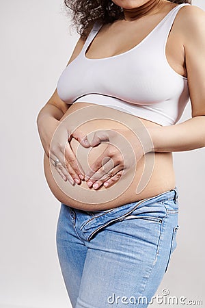 Closeup pregnant woman putting hands on naked belly, making heart shape from fingers. Happy carefree pregnancy 30 week Stock Photo