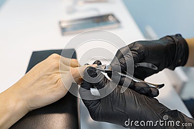 Closeup process of professional manicure. Manicurist woman hands in black gloves making manicure using professional tools. Nail Stock Photo