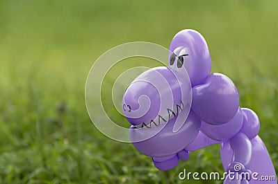 Closeup of purple balloon animal dinosaur in green grass of back Stock Photo