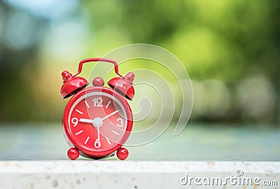 Closeup red alarm clock display seven hours and fifteen minutes on screen on blurred marble desk and park view background Stock Photo