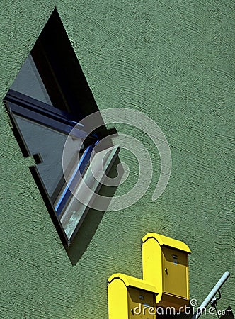 Closeup of a rhombus-shaped window and yellow postal boxes on the smooth green-painted exterior wall Stock Photo