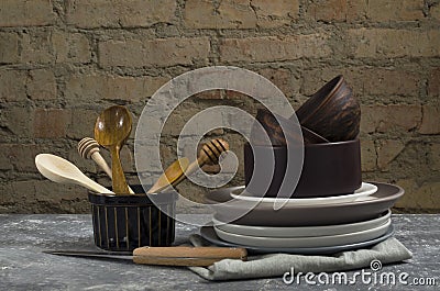 Closeup of rustic kitchenware, utensil on the table against old brick wall.Woodn spoons, clay and ceramic plates, bowls, napkin on Stock Photo