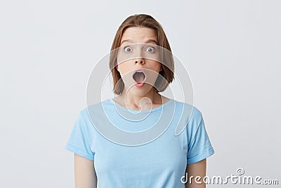 Closeup of shocked stunned young woman in blue t shirt with opened mouth feels amazed and looks directly in camera isolated over Stock Photo