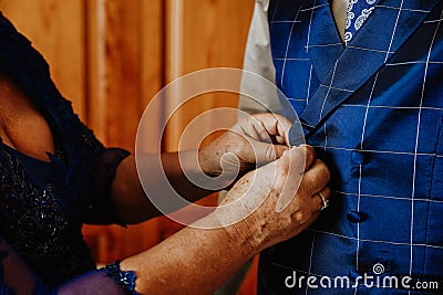 Closeup shot of aged female hands fastening buttons of a suit of his partner Stock Photo