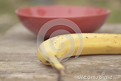 Closeup shot of a banana near a red bowl on a blurred background Stock Photo