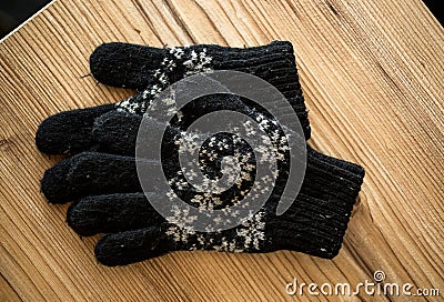 Closeup shot of black knitted gloves lying on wooden table Stock Photo