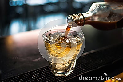 Closeup shot of blended whiskey being poured in a glass from a bottle with blurred background Stock Photo