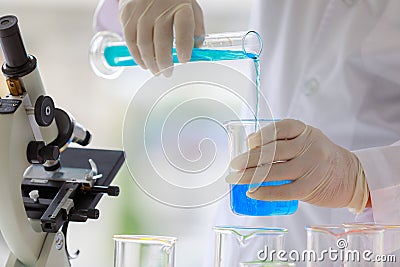 Closeup shot of blue reagent in glass volumetric cylinder poured in beaker by scientist in white lab coat and rubber gloves hands Stock Photo