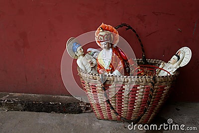 Closeup shot of Buddhist porcelain dolls in a straw basket in front of a red wall Stock Photo