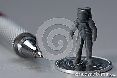 Closeup shot of a coin, a 3d printed astronaut figurine, and a pen on a white surface Stock Photo