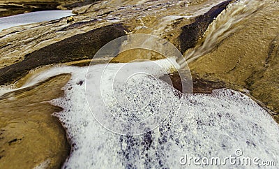 Closeup shot of the foam of the river flow on the brown rocks of the riverbank Stock Photo