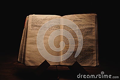 Closeup shot of a historic old Bible open on the Hebrews pages on display in a dark room Stock Photo