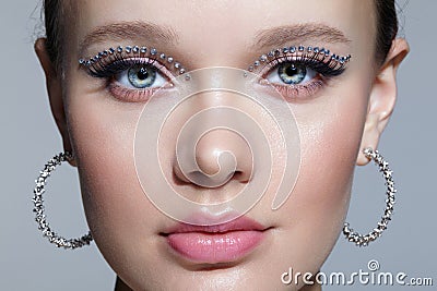 Closeup shot of human female face with unusual rhinestones makeup. Woman with earring in the form of a shiny ring in the ear Stock Photo