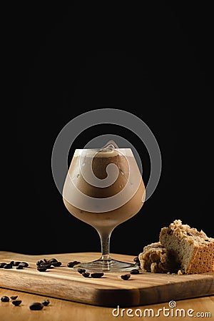 Closeup shot of an ice cappuccino glass on a wooden plate with decorations on a black background Stock Photo