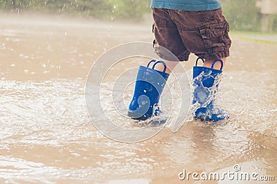 Closeup shot of the legs of a boy in blue rubber boots splashing in a puddle Stock Photo