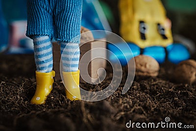 Closeup shot of the legs of a doll in striped socks and yellow rubber boots Stock Photo