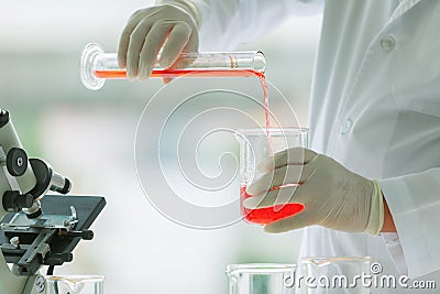 Closeup shot of orange red reagent in glass volumetric cylinder poured in beaker by scientist in white lab coat and rubber gloves Stock Photo