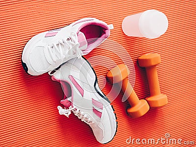 Closeup shot of pair of sports shoes, dumbbells and water tumbler isolated on orange surface Stock Photo