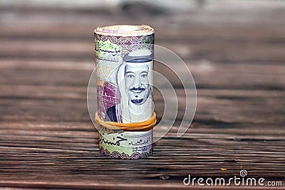 Closeup shot of a roll of 5 SAR ten Saudi riyals cash money banknote bills on a wooden table Stock Photo