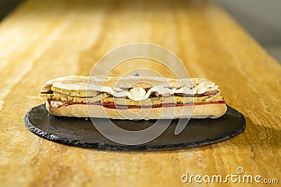 Closeup shot of a sandwich with mayonnaise on a black round board on a wooden surface Stock Photo