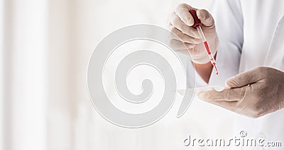 Closeup shot of scientist wears white lab coat and rubber gloves hands holding orange red reagent in glass dropper dropping into Stock Photo