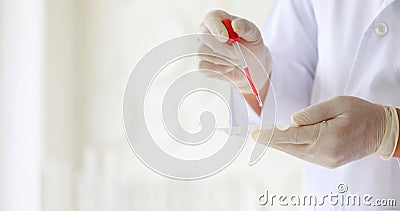 Closeup shot of scientist wears white lab coat and rubber gloves hands holding orange red reagent in glass dropper dropping into Stock Photo