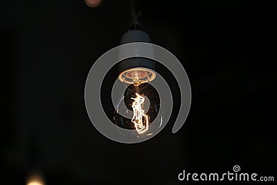 Closeup shot of a single electric lamp with softly glowing metal filament hanging on a cable Stock Photo