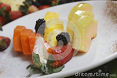 Closeup shot of sliced pineapple, papaya, melon, strawberries, and blackberries on a plate Stock Photo