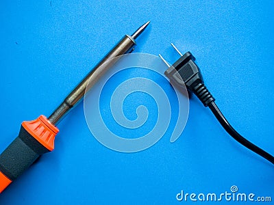 Closeup shot of a soldering iron and a black American plug on a blue surface Stock Photo