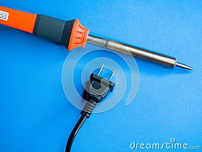 Closeup shot of a soldering iron and a black American plug on a blue surface Stock Photo