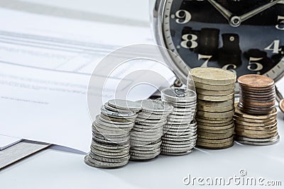 Closeup shot of stacks of coins near a clock Stock Photo