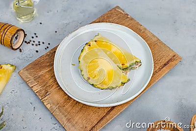 Closeup shot of two pieces sliced yellow pineapples on white dish on wood cutting board placed on table with other ingredients Stock Photo