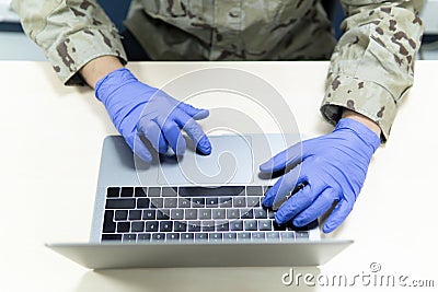 Closeup shot of uniformed military male with medical gloves using his laptop Stock Photo