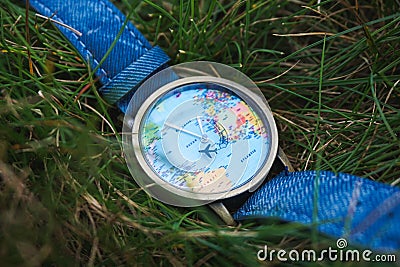 Closeup shot of a watch with a design of the world map on the grassy terrain Editorial Stock Photo