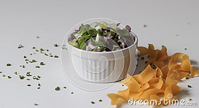 Closeup shot of a white bowl of a vegetable salad with raw pasta on the side on a white surface Stock Photo