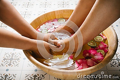 Closeup shot of a woman feet dipped in water with petals in a wooden bowl. Stock Photo