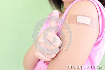 Closeup of shoulder of a vaccinated young Asian girl with adhesive bandage in thumbs up. Young people, children covid vaccination. Stock Photo