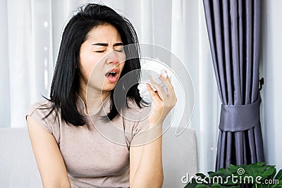 Sick Asian woman sneezing hand holding paper tissue having flu, runny nose caused of cold , allergy to dust Stock Photo