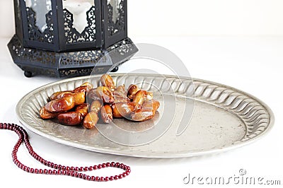 Closeup of silver plate with date fruits, prayer beads and ornamental dark Moroccan, Arabic lantern on the white table Stock Photo