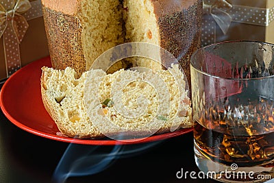 Closeup of a slice of panettone under cigarette smoke, next to a glass of whiskey side view Stock Photo