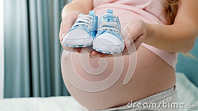 Closeup of small blue newborn baby boots on hands of yougn pregnant woman Stock Photo