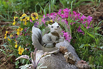 Closeup of a small squirrel statue on a rock in a garden covered in flowers Stock Photo